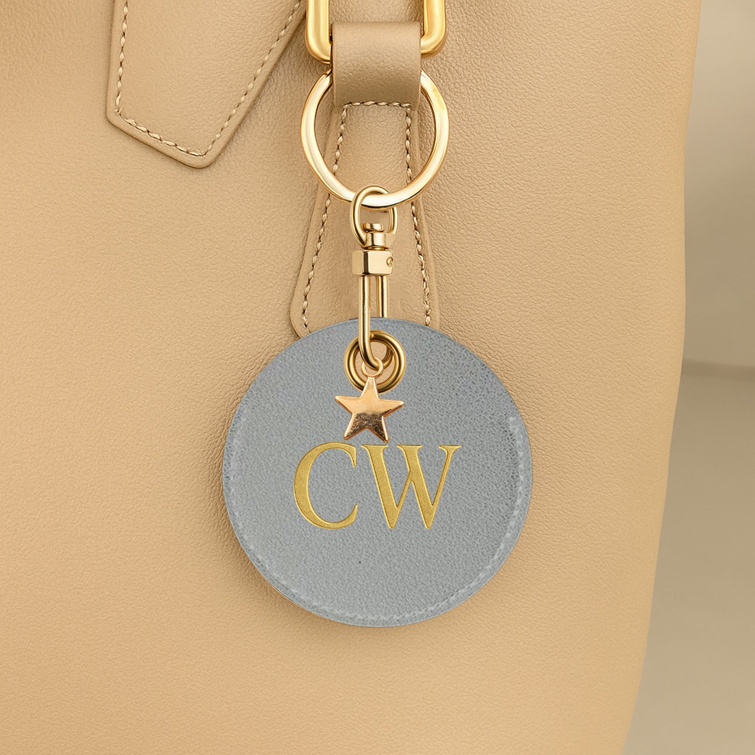 Gray keychain with gold initials attached to a beige bag