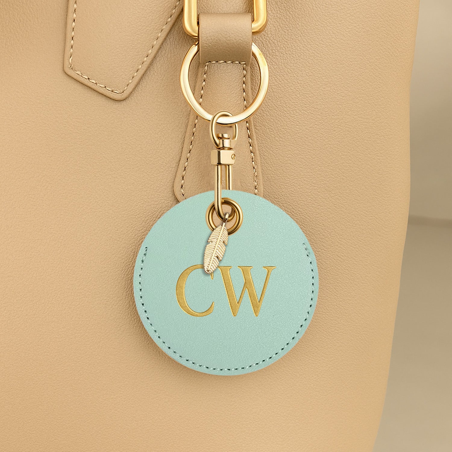 Round turquoise keychain with 'CW' initials attached to a beige bag.