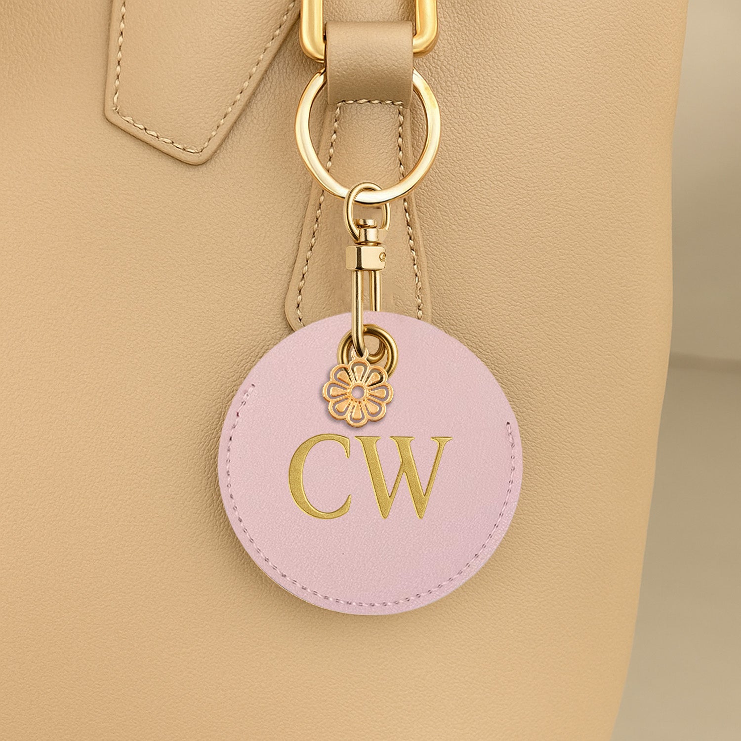 Pink keychain with gold initials attached to a beige handbag