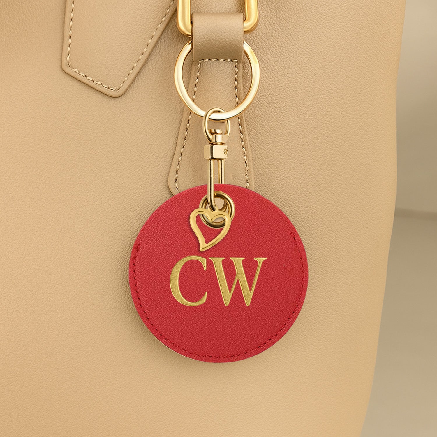 Red leather keychain with gold initials attached to a beige handbag