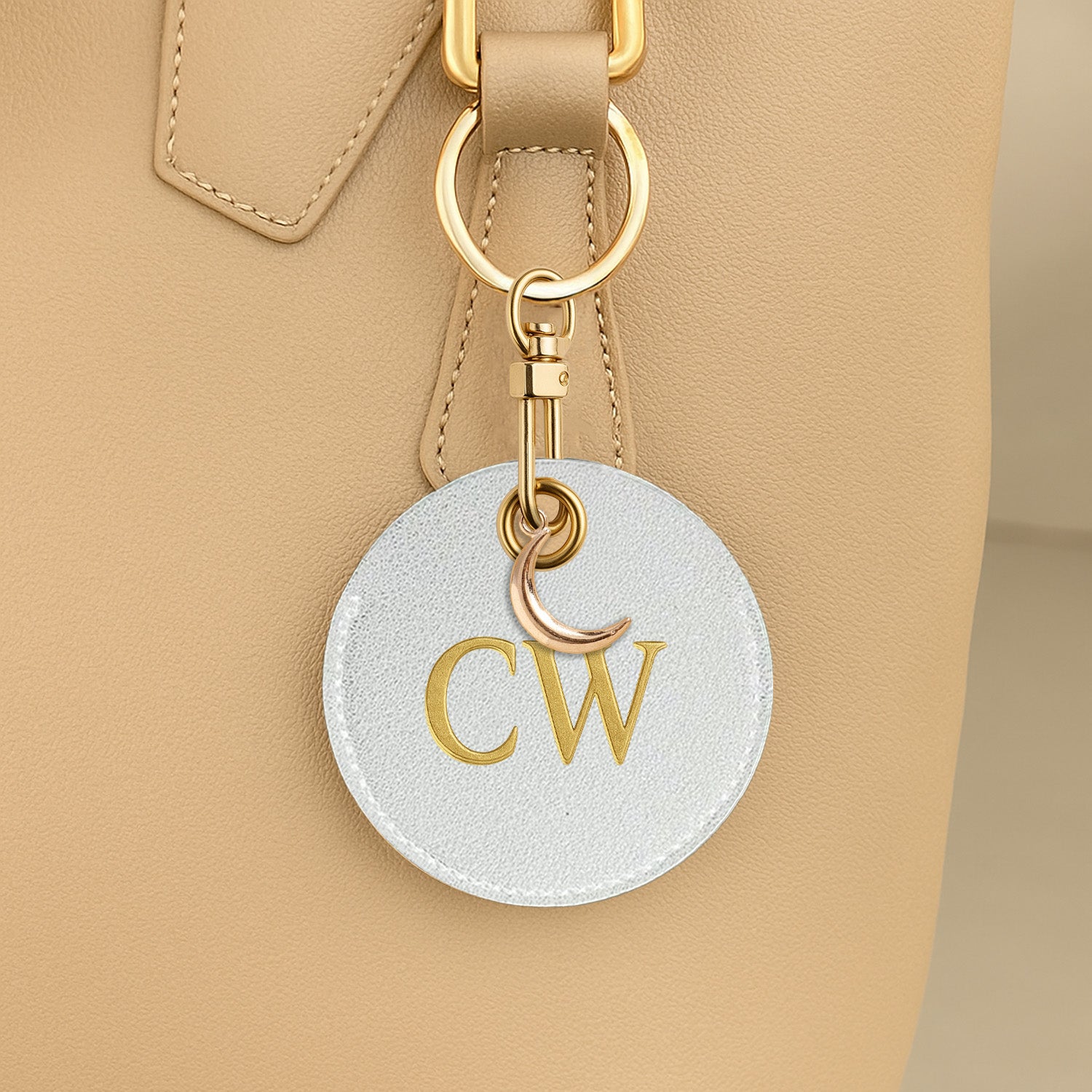 Round keychain with 'CW' initials attached to a beige handbag.