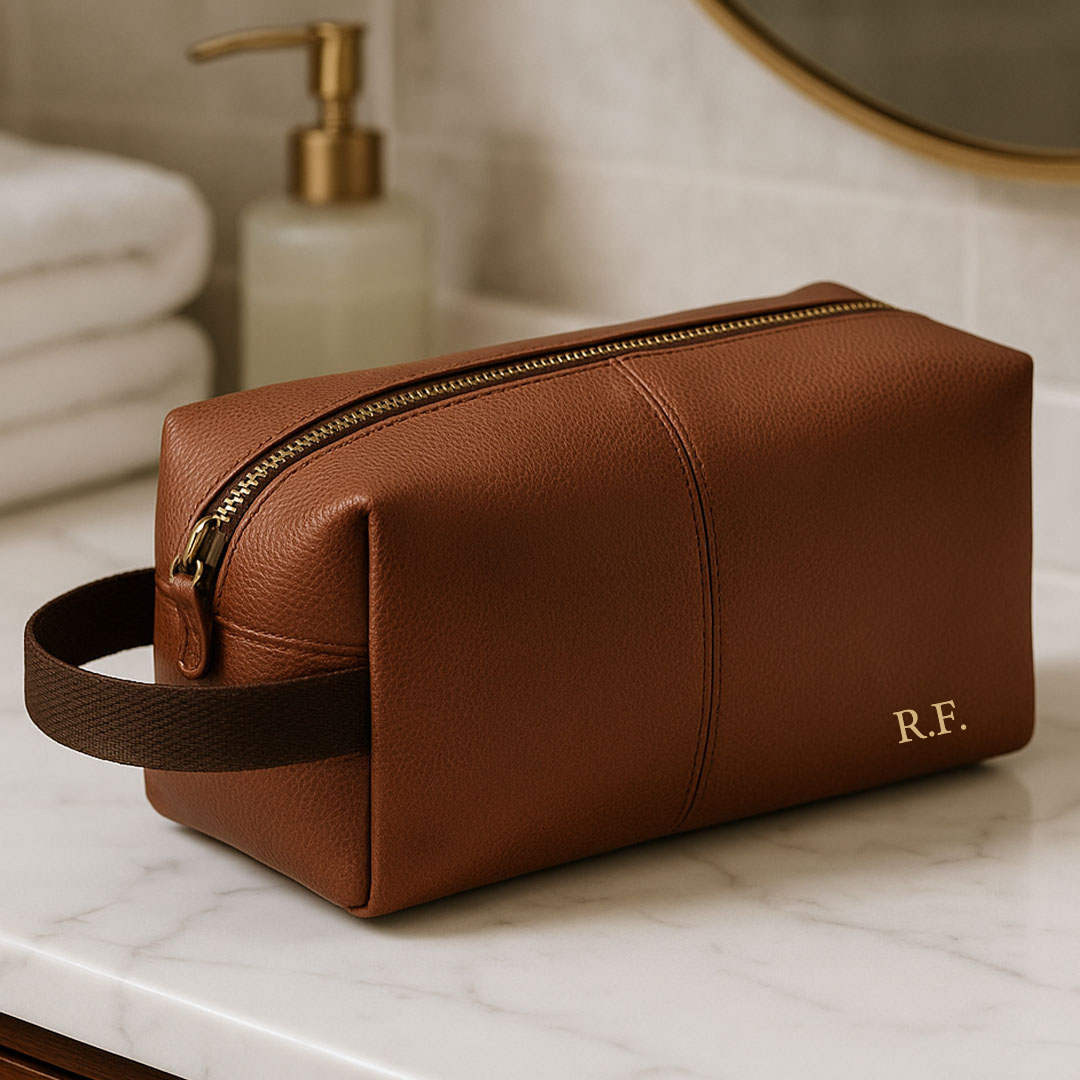 Brown leather toiletry bag with gold zipper on a marble surface, blurred bathroom background
